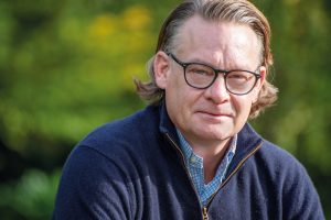 Anwalt Stefan Gelhaus mit Brille vor grünem Hintregrund